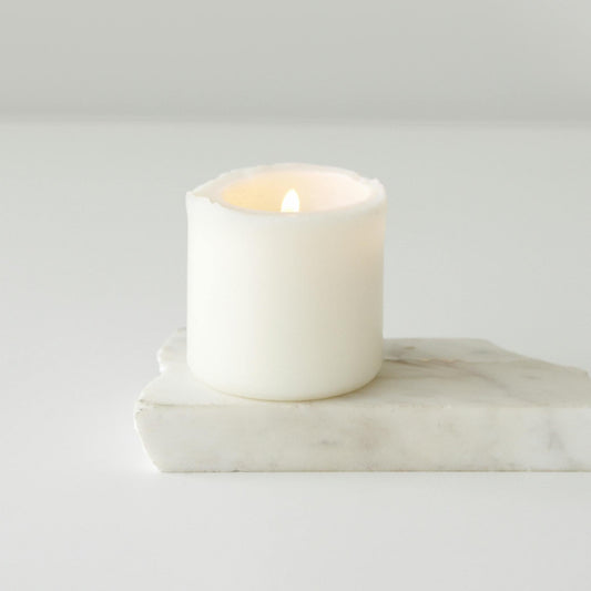 A white electronic candle with a warm glow, placed on a marble surface.