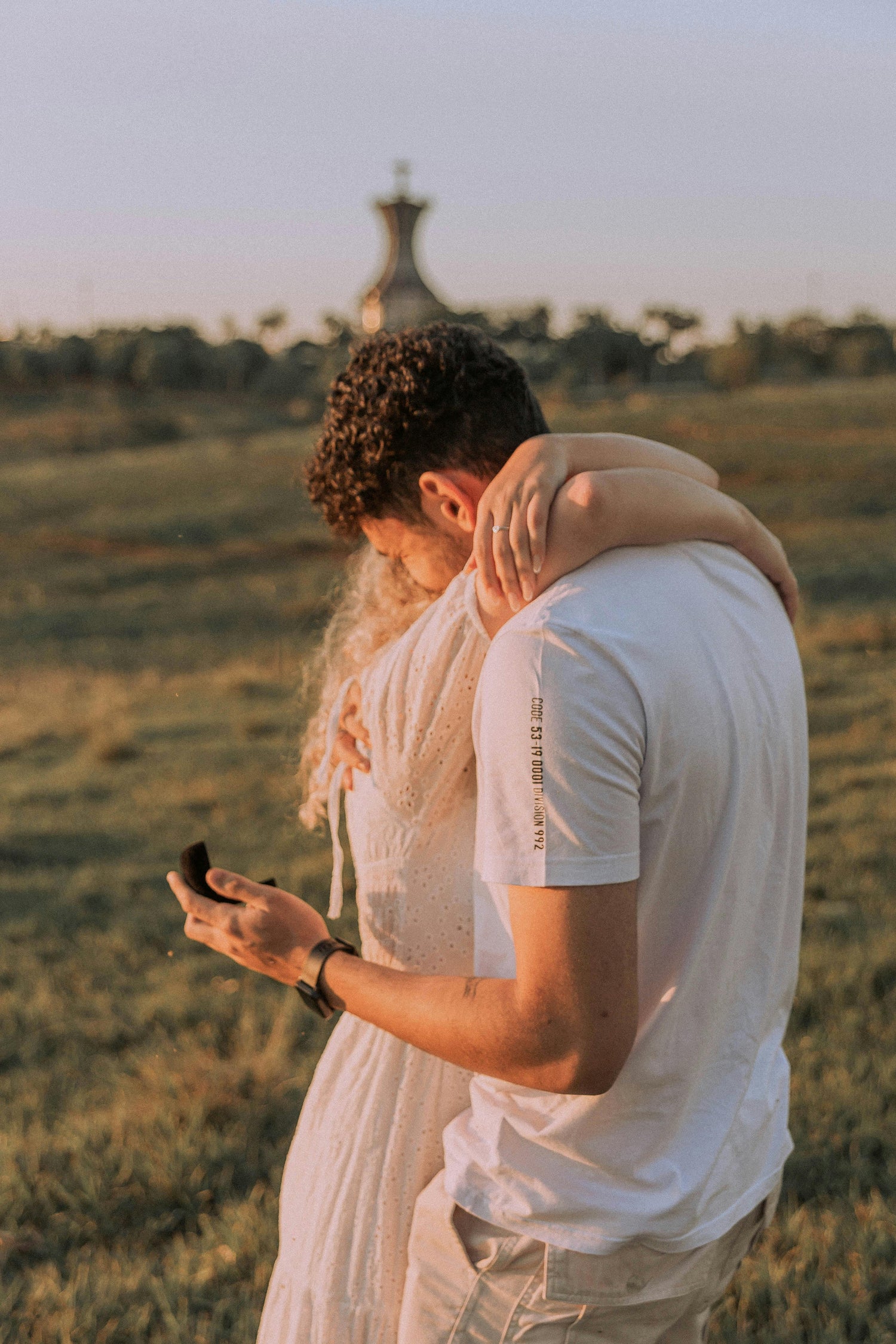 Two people embracing in a field with a scenic background