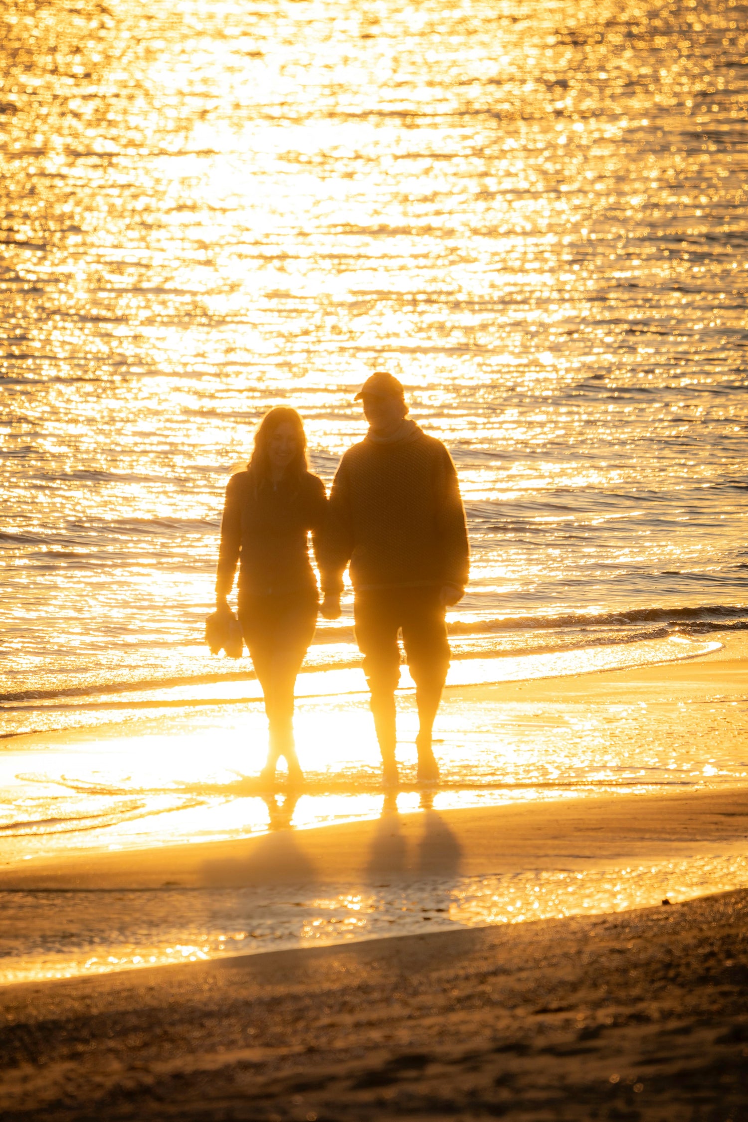 Two people walking on a beach at sunset, silhouetted against the glowing water.