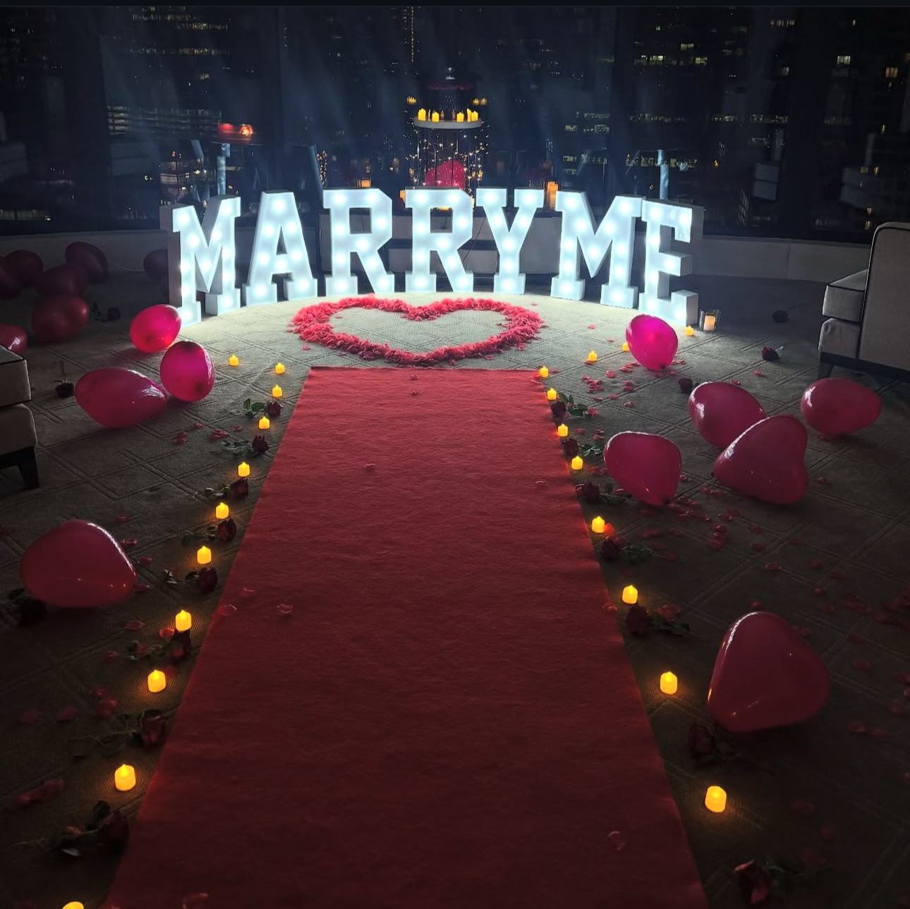 Proposal setup with 'MARRY ME' sign on a red carpet at night.