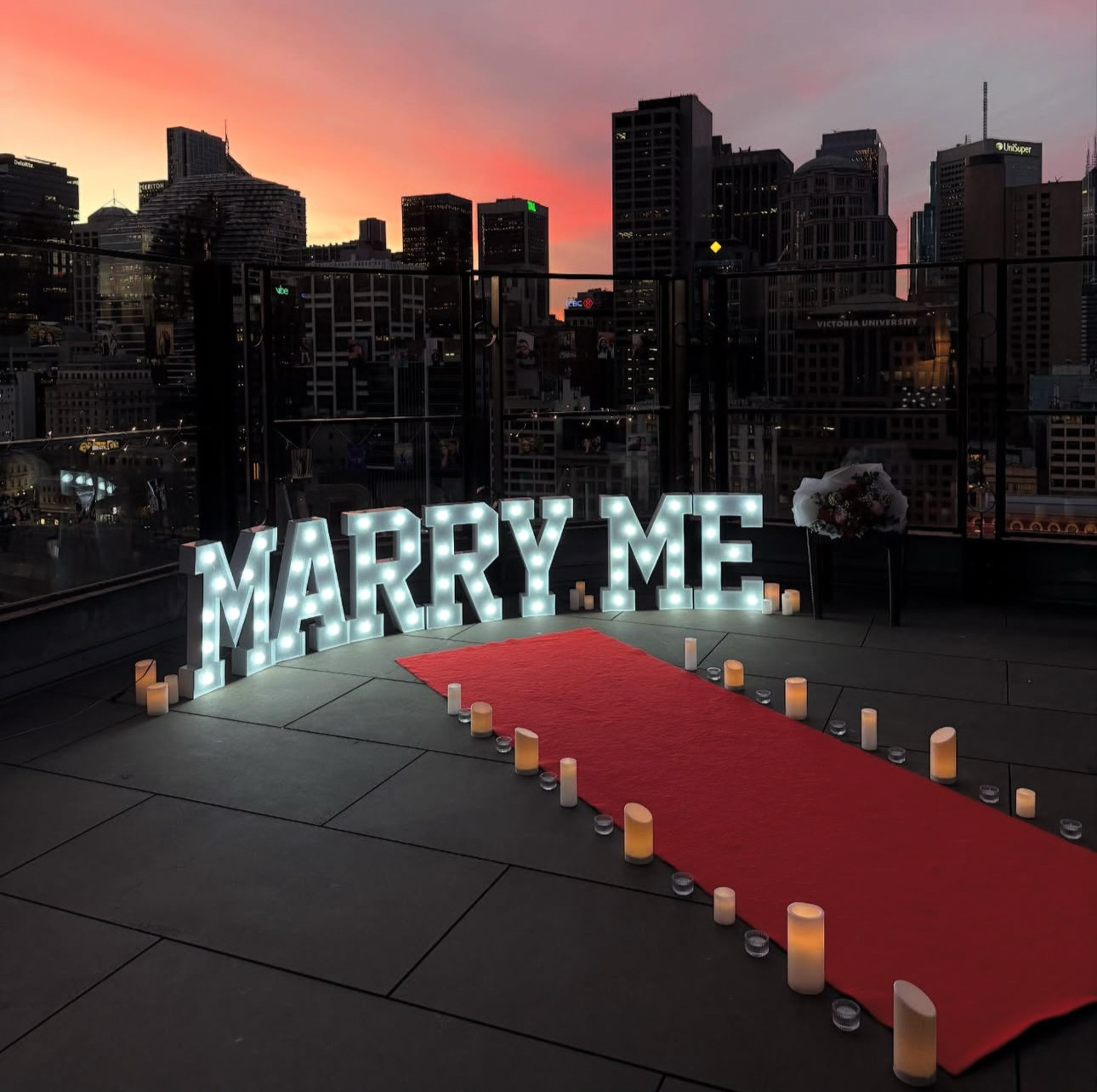 Proposal setup with 'MARRY ME' sign on a red carpet in an urban setting