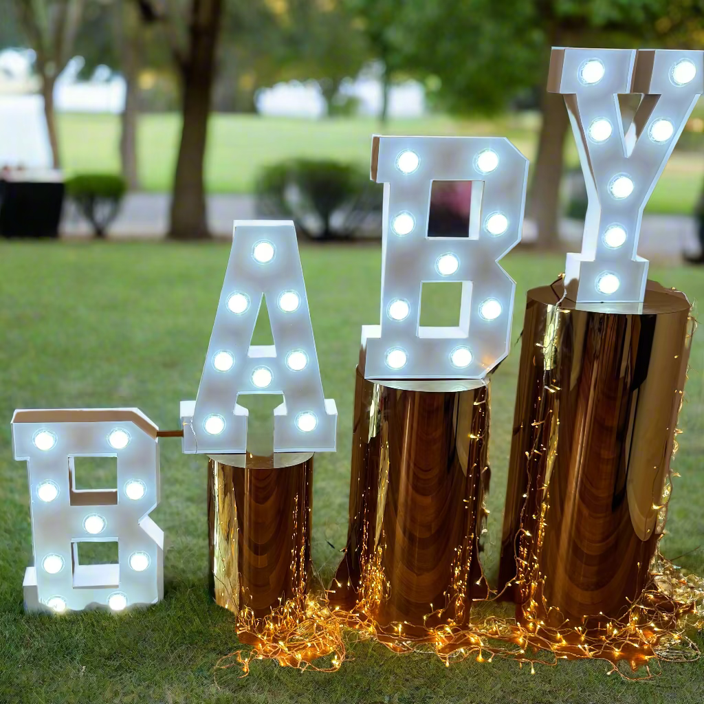 Decorative setup with 'BABY' letters, teddy bear, and fairy lights on a wooden floor.