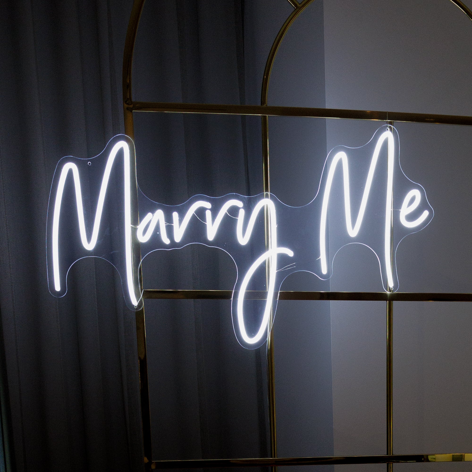 An LED neon sign with the phrase 'Marry Me' written in elegant cursive script, emitting a soft white glow.