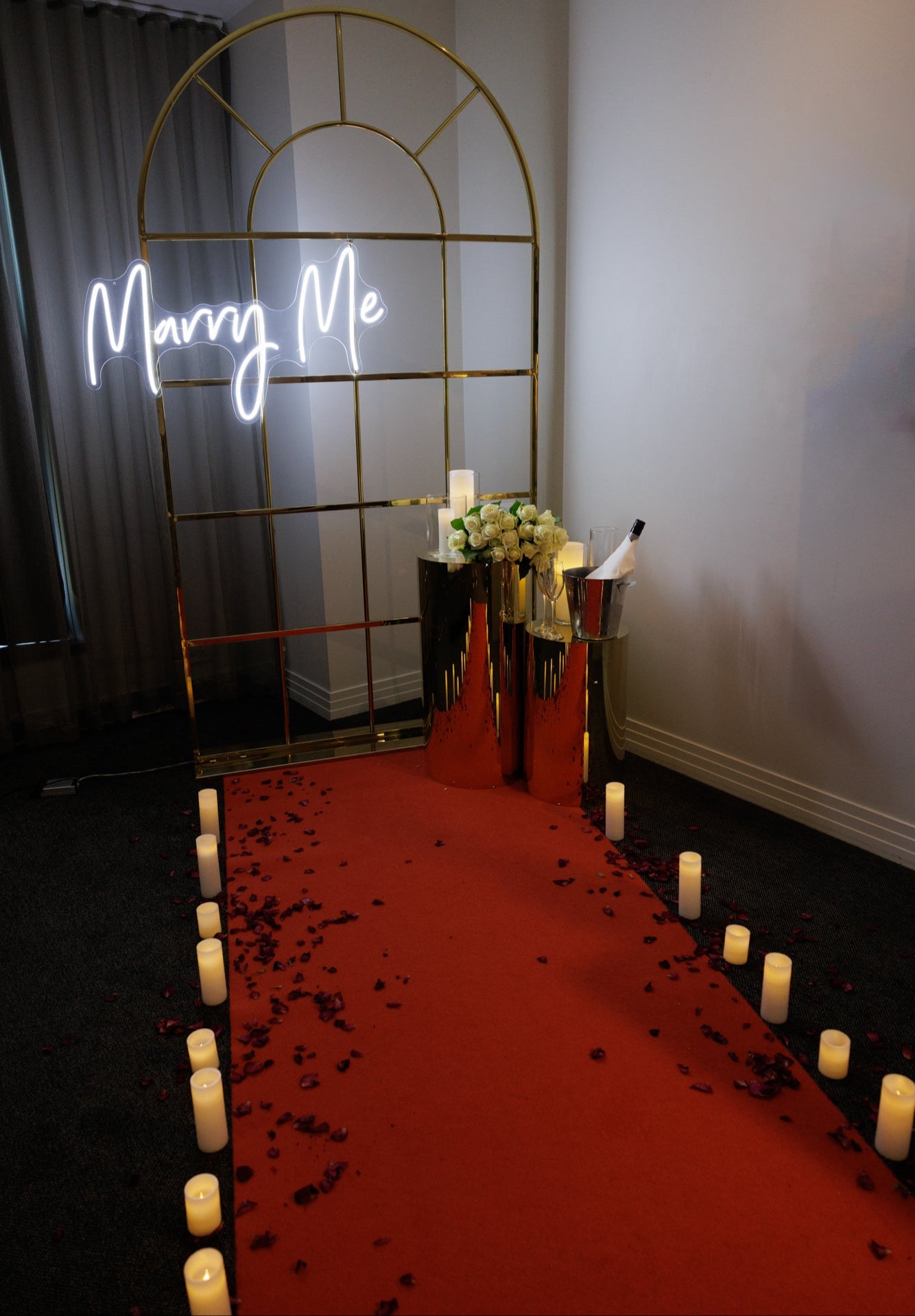 Decorated room with a red carpet, candles, and 'Marry Me' sign.