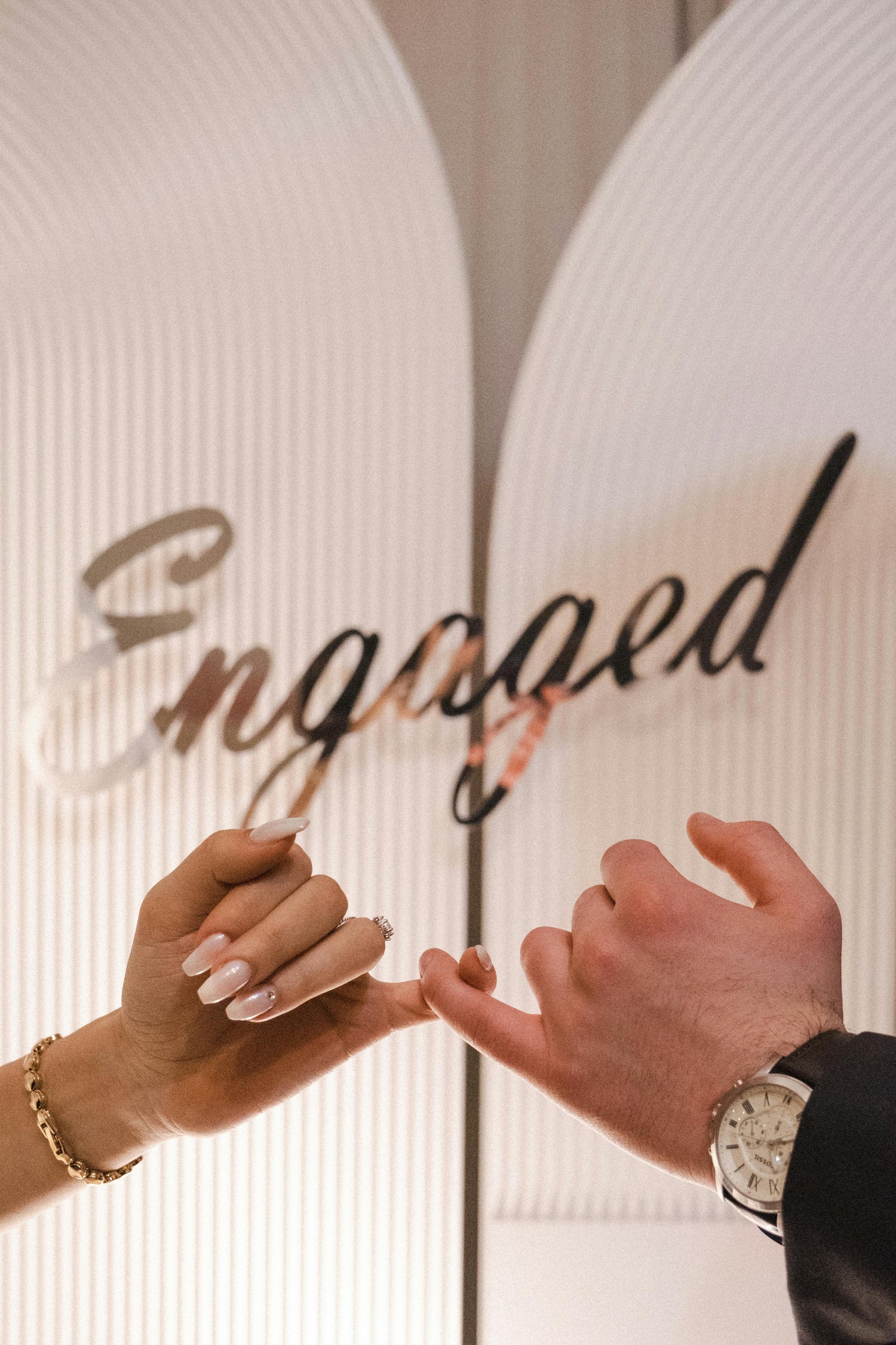 Two people holding hands with 'Engaged' text in the background