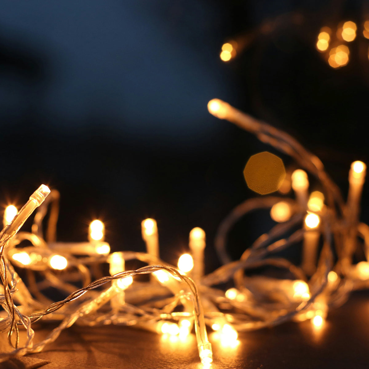 A close-up of warm white LED fairy lights on a clear string, showing the lights glowing in a dark environment.