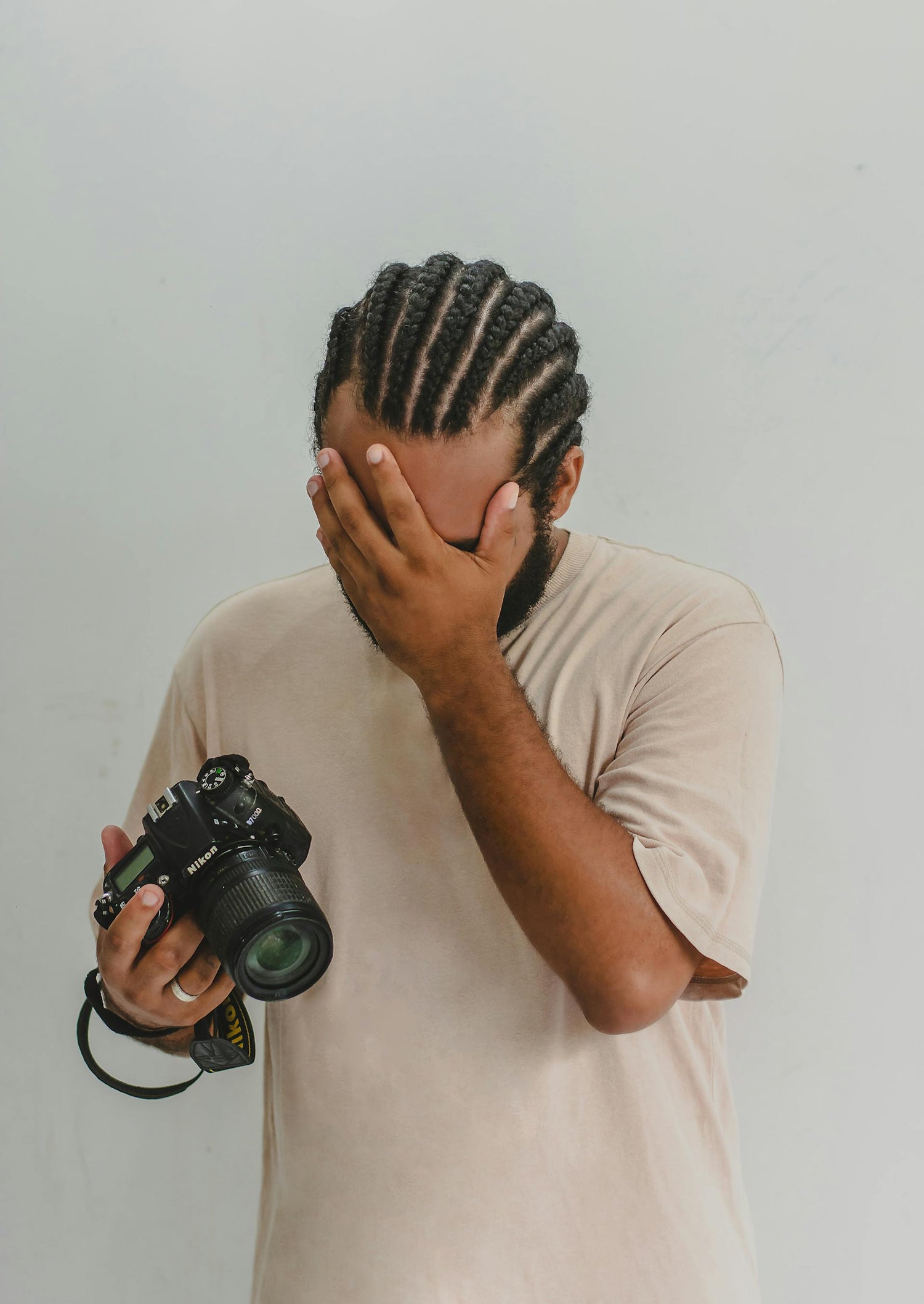 Person holding a camera with one hand and covering their face with the other, against a plain background
