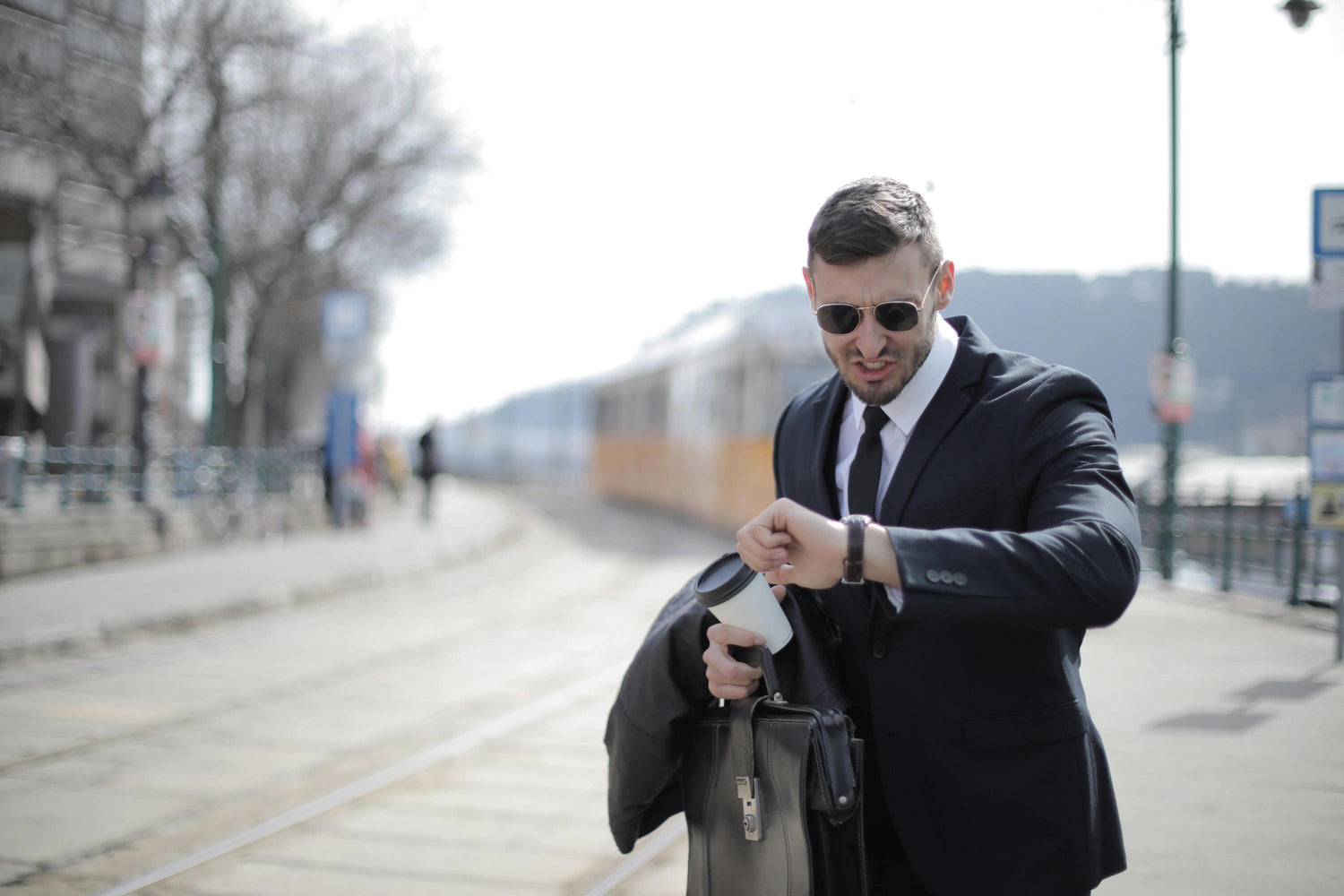 Man in a suit and sunglasses checking his watch at a train station.