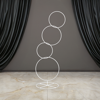 A white round hoop backdrop stand with multiple circular hoops, placed on a base, with curtains in the background.